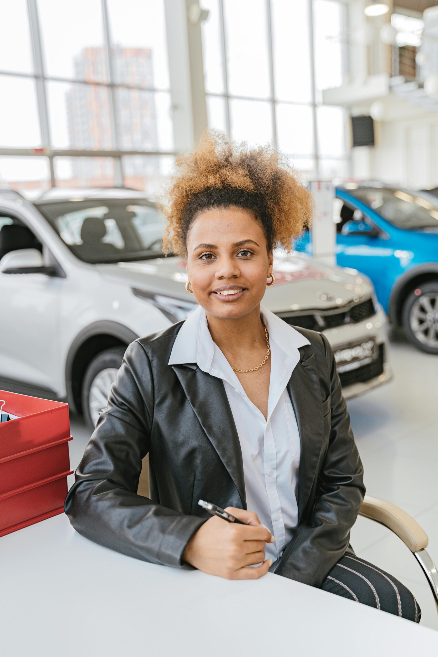 African American woman smiling confidently in car showroom, representing automotive sales.